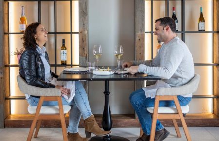 A couple smiling and enjoying a seasonal lunch at the best restaurant in Requena with wine glasses and vineyard views.