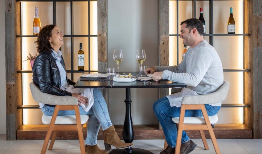 A couple smiling and enjoying a seasonal lunch at the best restaurant in Requena with wine glasses and vineyard views.
