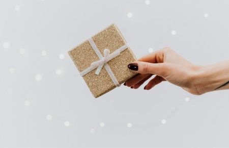 Mano entregando un pequeño regalo de Navidad dorado con lazo blanco. Ideas para regalar experiencias de enoturismo para amantes del vino.