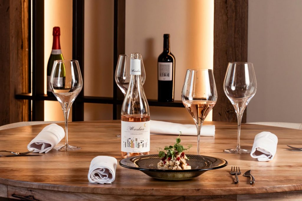 Mesa de madera con entrante y copas maridadas con vino Mariluna rosado Garnacha y Bobal, en el restaurante de la bodega Finca Calderón en Requena