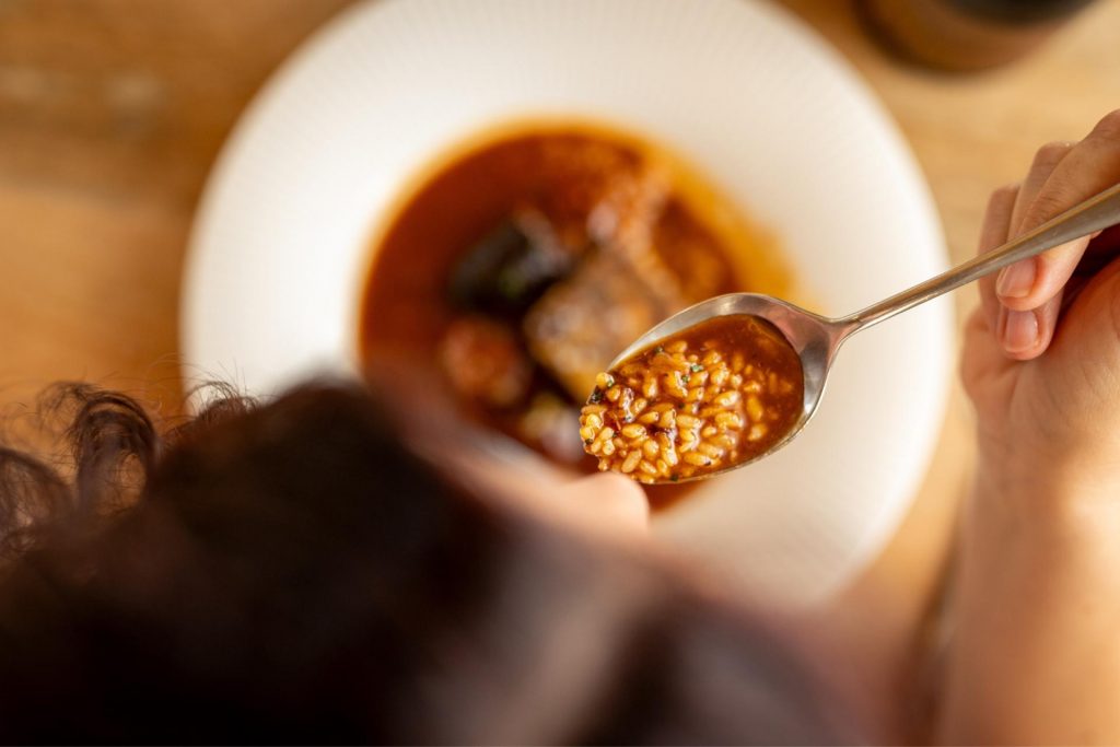 Vista cenital de una persona degustando un plato de arroz meloso maridado con vino en el restaurante Finca Calderón, en Requena, Valencia.