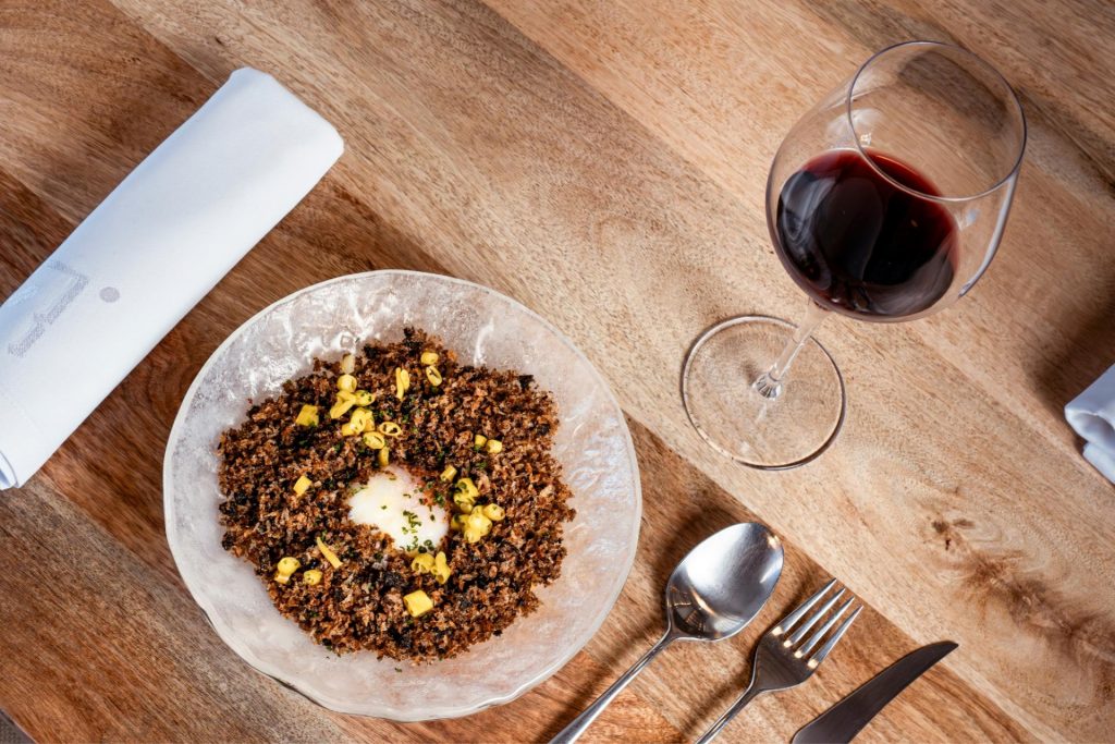 Vista superior de mesa con plato del menú gourmet acompañado de copa de vino tinto en el restaurante de la bodega Finca Calderón en Requena