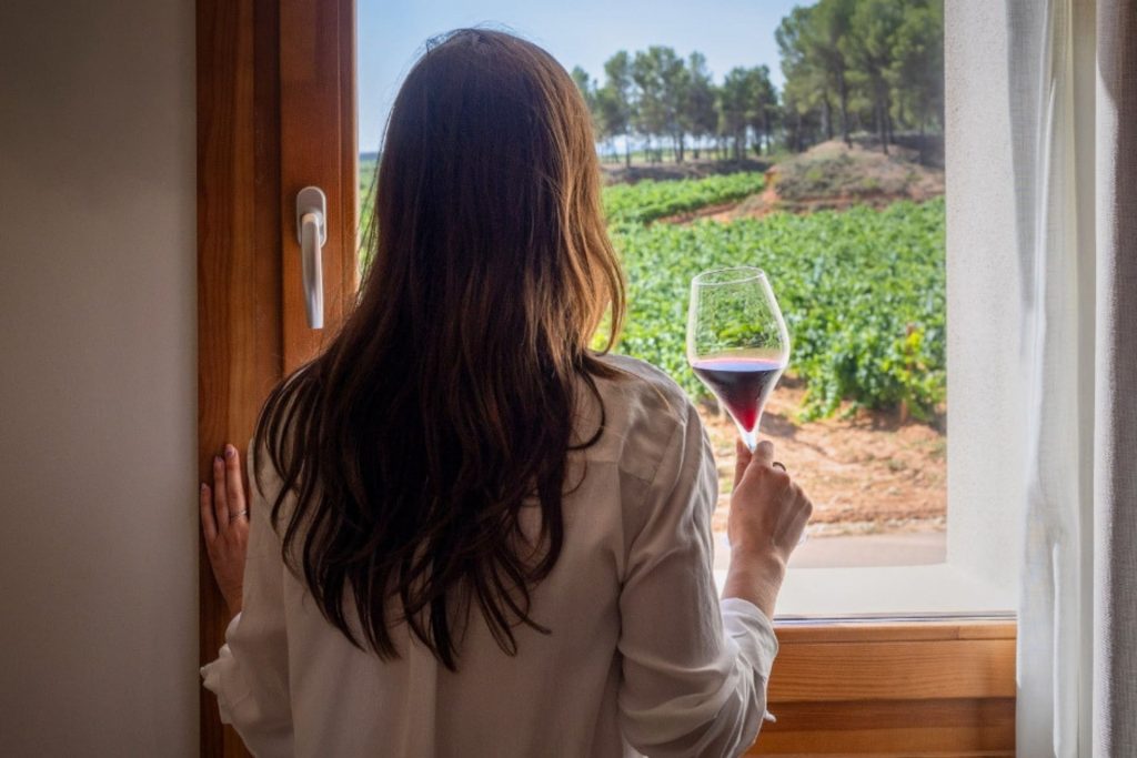 Mujer mirando por la ventana del hotel entre viñedos y bodega finca calderon, en requena, provincia de valencia.